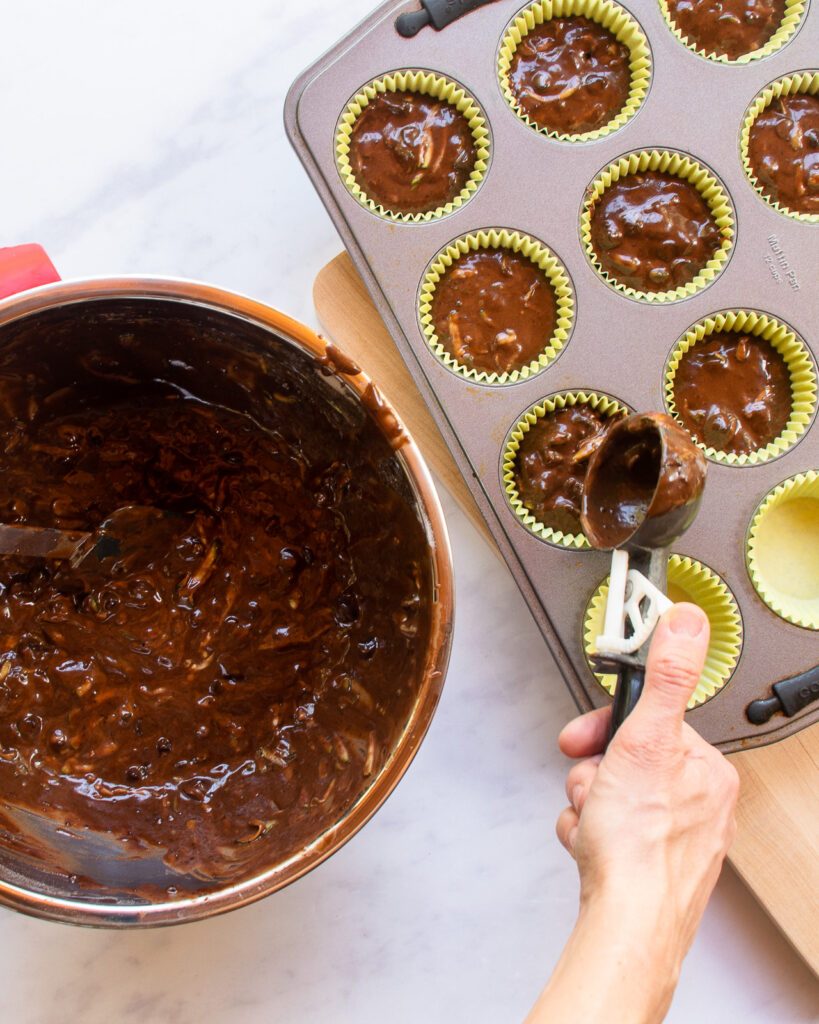A hand scooping muffin batter into a muffin pan.