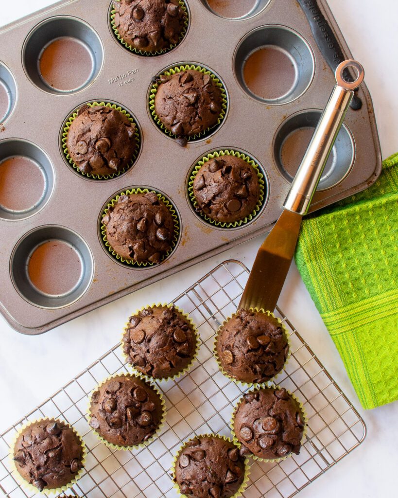 An offset spatula taking muffins out of a muffin pan and placing them on a cooling rack.