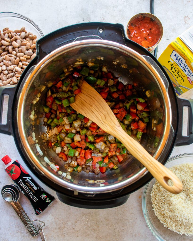 Looking down into a pressure cooker with vegetables in the bottom and a wooden spoon sticking out.
