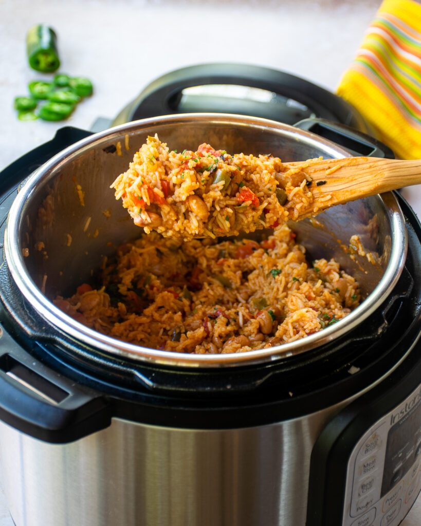 A wooden spoon lifting mexican rice and beans out of a pressure cooker.