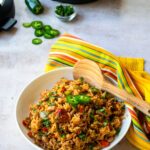 Mexican rice and beans in a white bowl with wooden spoon and yellow kitchen towel.