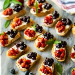 Rows of Berry and Goat Cheese Crostini on a marble surface with blueberries and napkins.