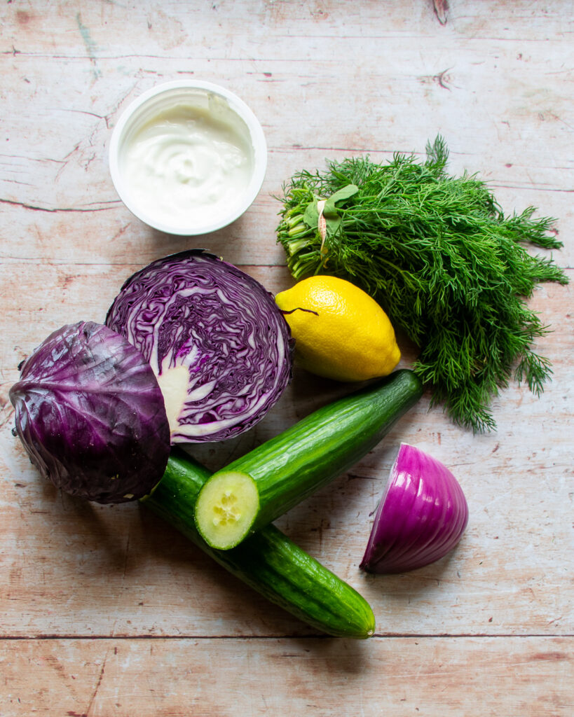 Vegetables on a wooden countertop - red cabbage, red onion, cucumber, lemon, dill and yogurt.