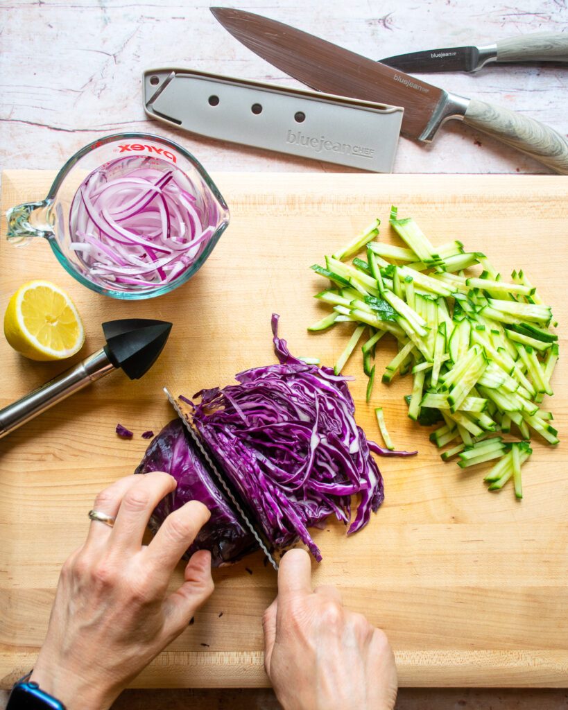 Hands cutting red cabbage on a wooden cutting board.