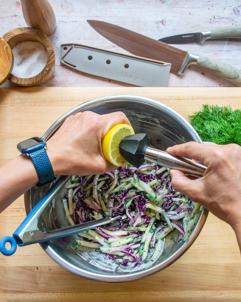 Hands reaming a lemon into a bowl of cucumber slaw.