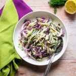 Cool Cucumber Slaw in a white bowl with purple and green napkins near by.