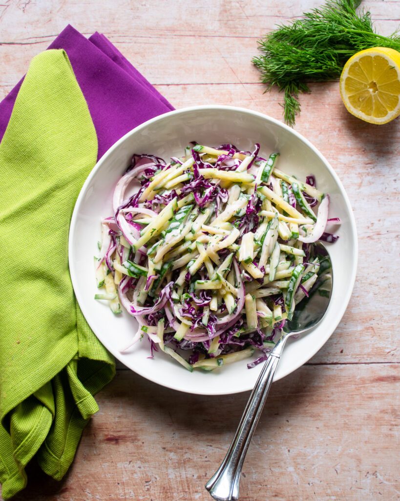 Cool Cucumber Slaw in a white bowl with purple and green napkins near by.