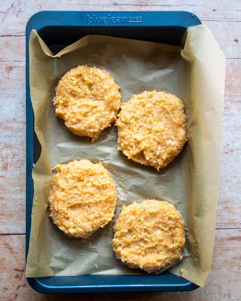 4 chicken burger patties in a parchment lined baking pan.