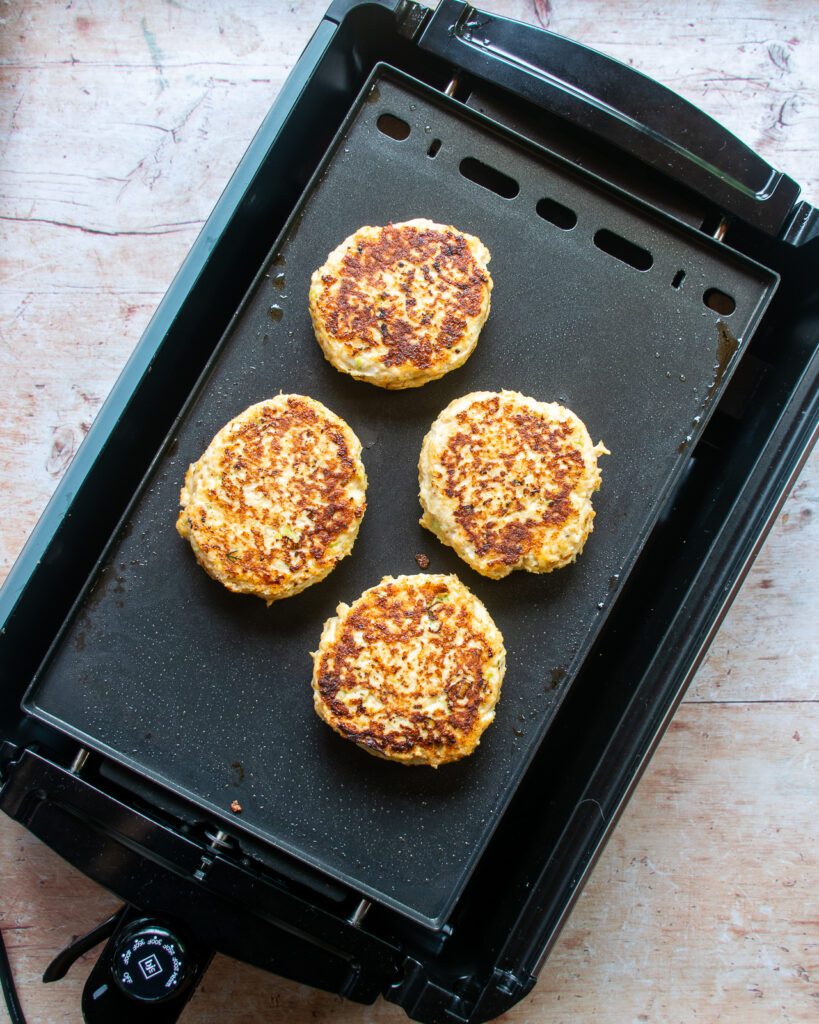 4 chicken burger patties cooking on an electric griddle.