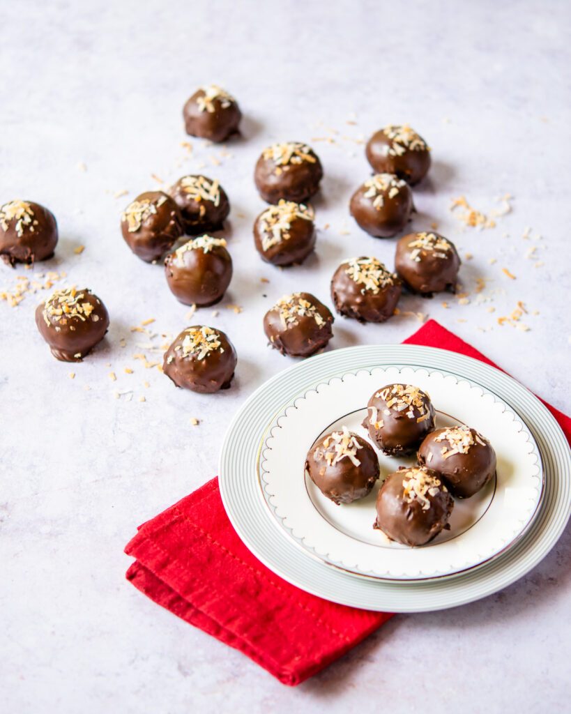 A small plate with a stack of chocolate toasted coconut balls on a red napkin with more balls in the background.