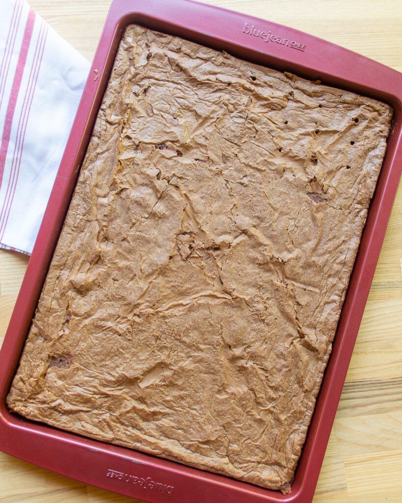 A sheet pan with chocolate brownie and a red and white striped towel.