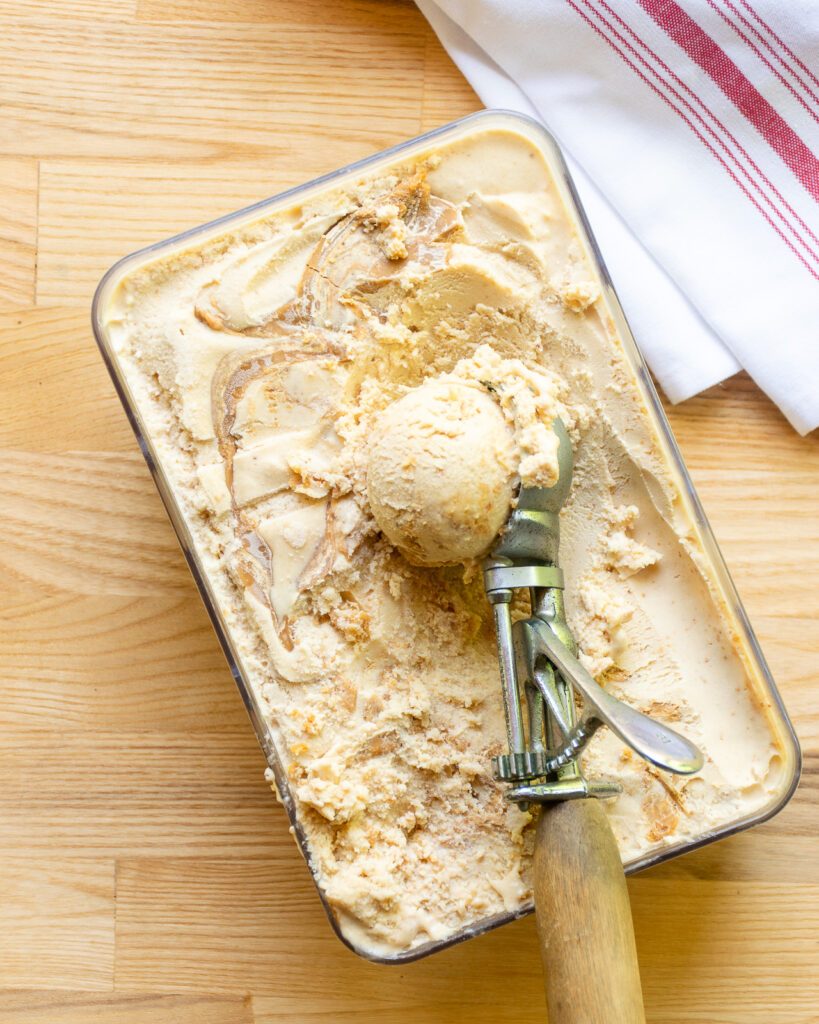 A wooden handled ice cream scoop scooping peanut butter swirl ice cream.