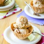 Peanut butter swirl ice cream in a waffle cup with a pink napkin and more ice cream in the background.