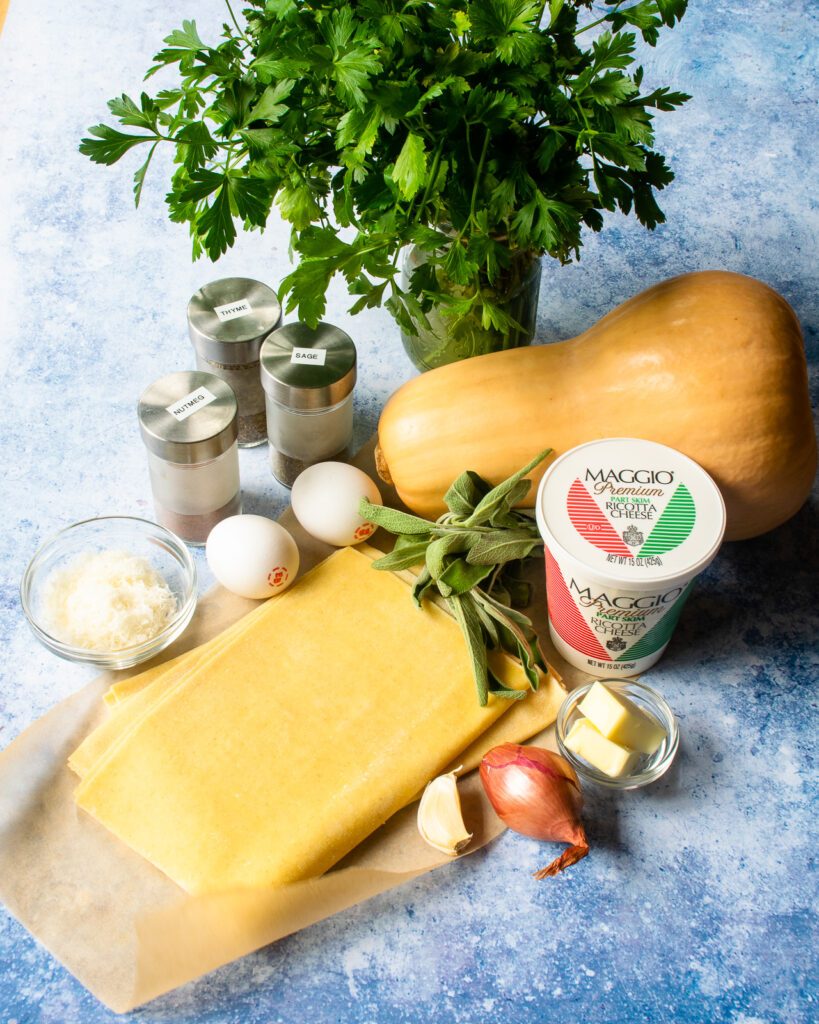 Ingredients on a countertop - pasta sheets, shallot, ricotta cheese, sage, parsley, eggs and butternut squash.