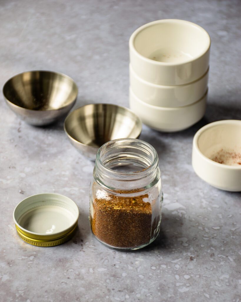 A jar of taco seasoning with empty white bowls nearby.