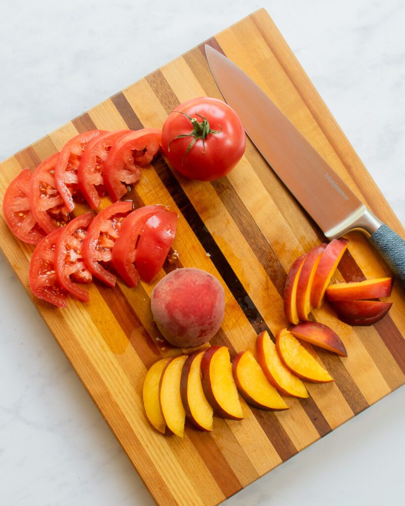 Tomatoes and peaches sliced on a cutting board with a chef's knife.