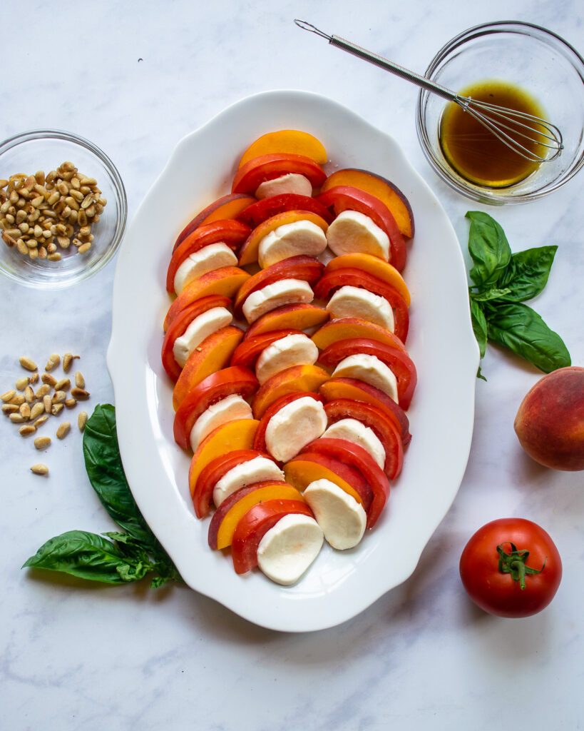 Peach Caprese sald being assembled on a white oval platter.