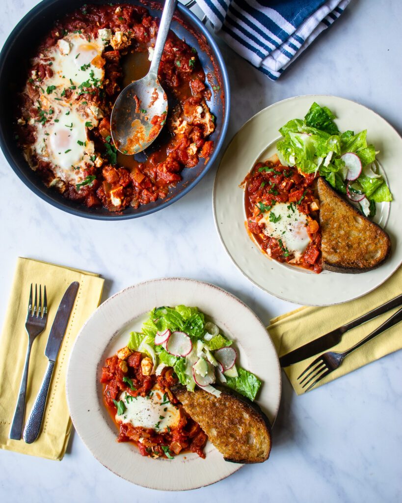 Looking straight down on two plates of shakshuka with salad and toast.