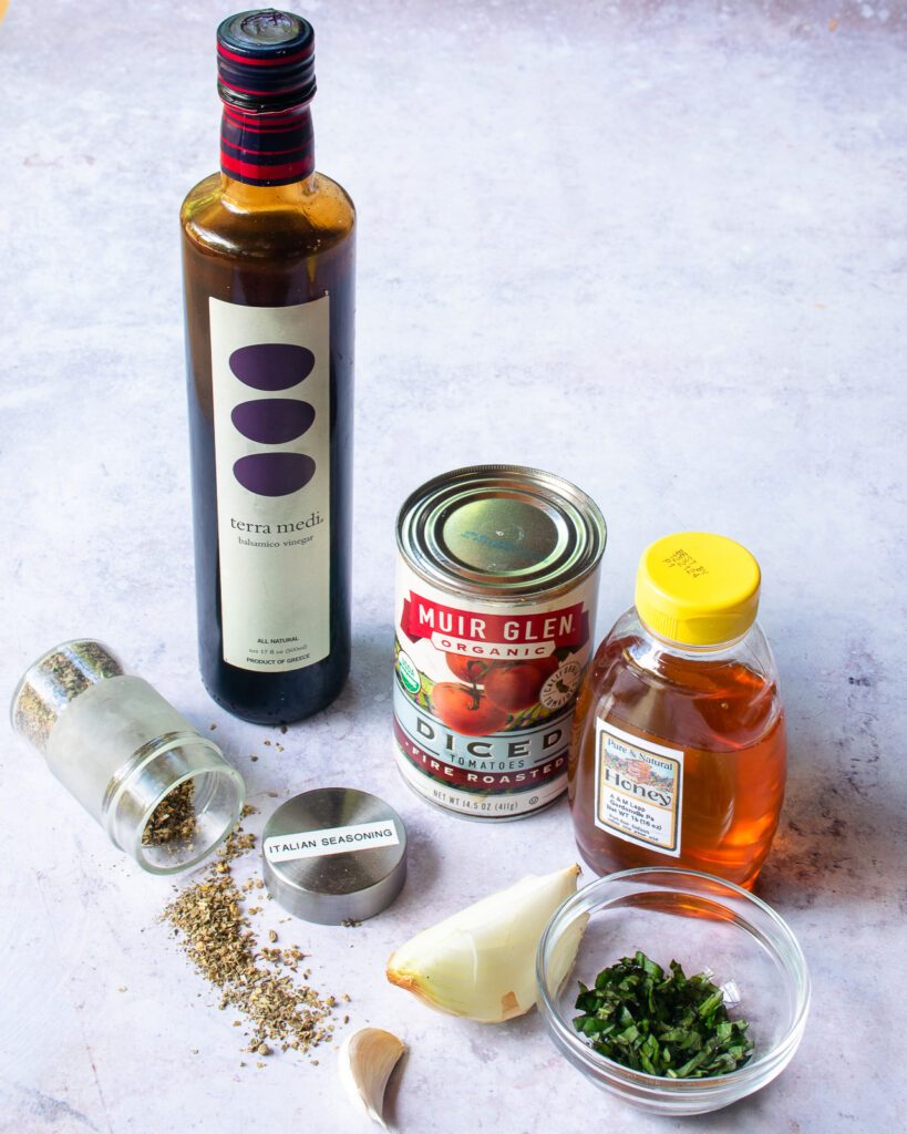 Ingredients on a counter - balsamic vinegar, honey, fire-roasted tomatoes spices, onion, garlic and parsley.