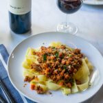 A plate of pappardelle noodles with bolognese sauce, wine and table setting.