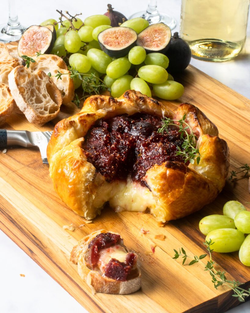 Baked brie with fig jam on a serving board with a wedge cut out.