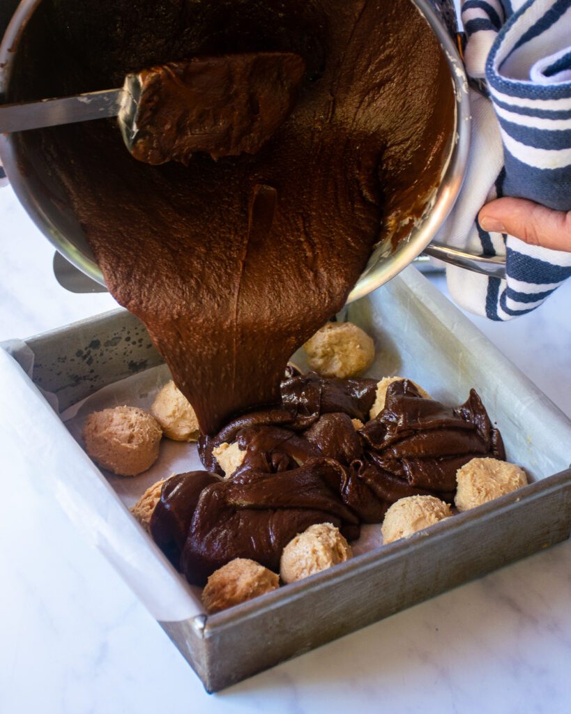 Pouring chocolate fudge over peanut butter balls in a square baking dish.