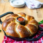 Cheese Stuffed Bread Ring in a cast iron vertical roaster with a red kitchen towel and some plates in the background.