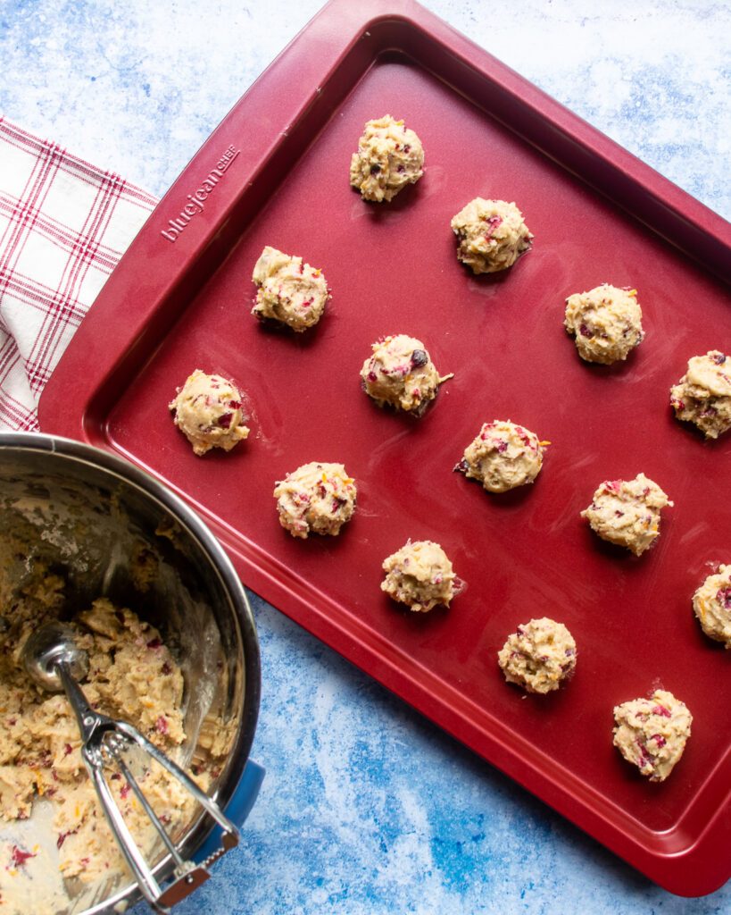 Raw cookie dough on a red baking sheet with a red and white kitchen towel near by.
