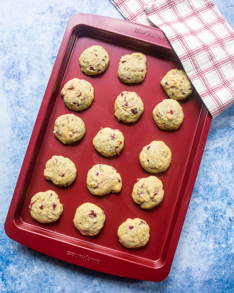 Baked cookies on a red baking sheet with a red and white kitchen towel on one corner.