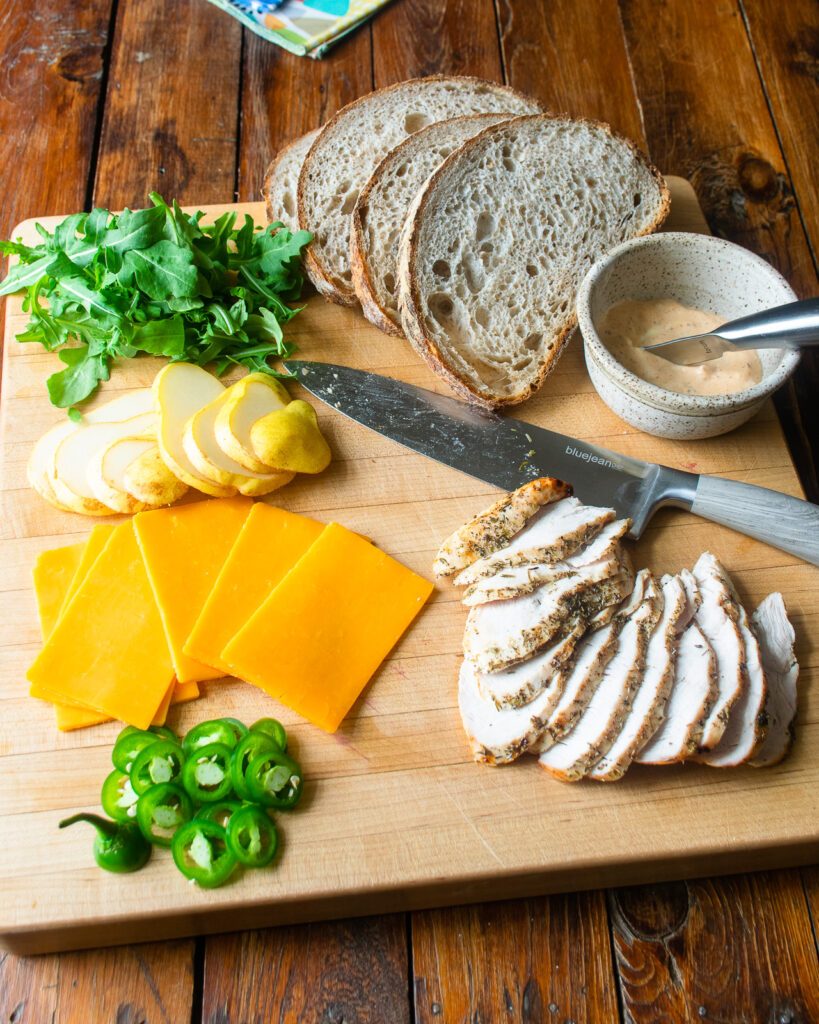A cutting board with the ingredients for a spicy turkey panini on it.