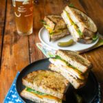 Two spicy turkey paninis on plates with a glass of beer.
