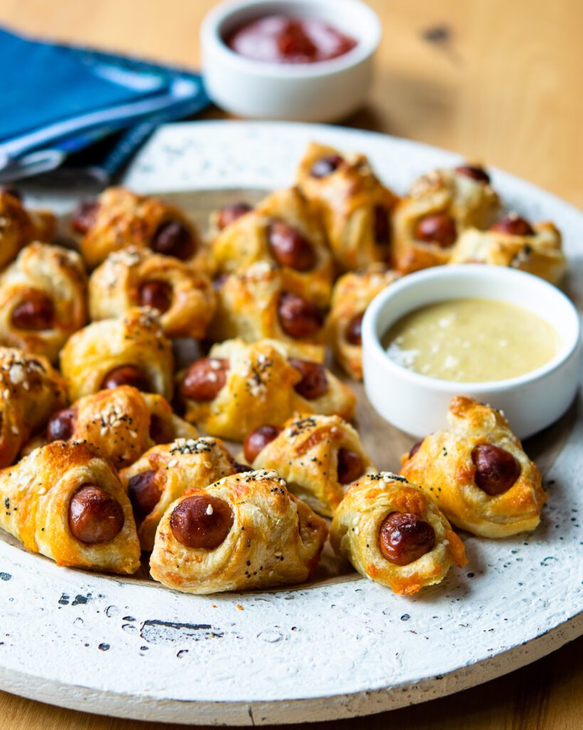 Cheesy Pigs in a Blanket on a white platter with honey mustard.