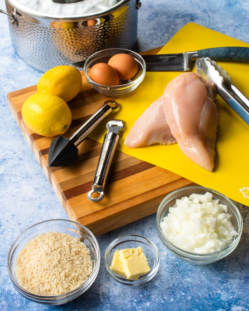 Ingredients on a cutting board - lemons, eggs, diced onion, rice, butter and chicken breasts.
