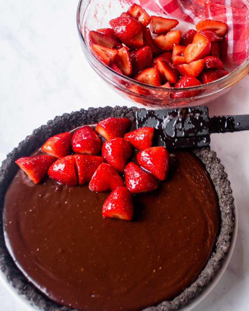 Glazed strawberries being placed on a chocolate tart.