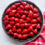 Looking straight down on a strawberry chocolate tart with a red and white towel near by.