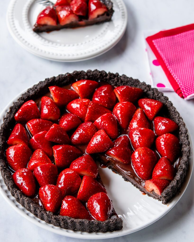 A large chocolate strawberry tart with a slice cut out of it.