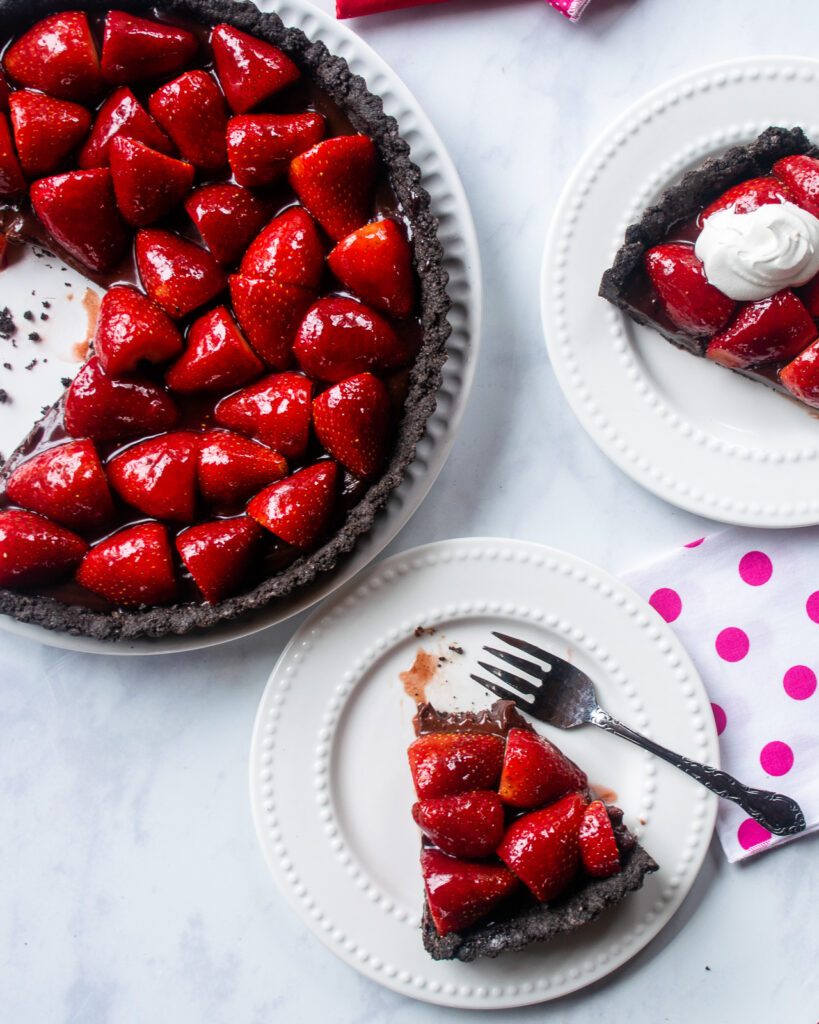 Two small white plates with a slice of chocolate strawberry tart on each one and the rest of the large tart nearby.