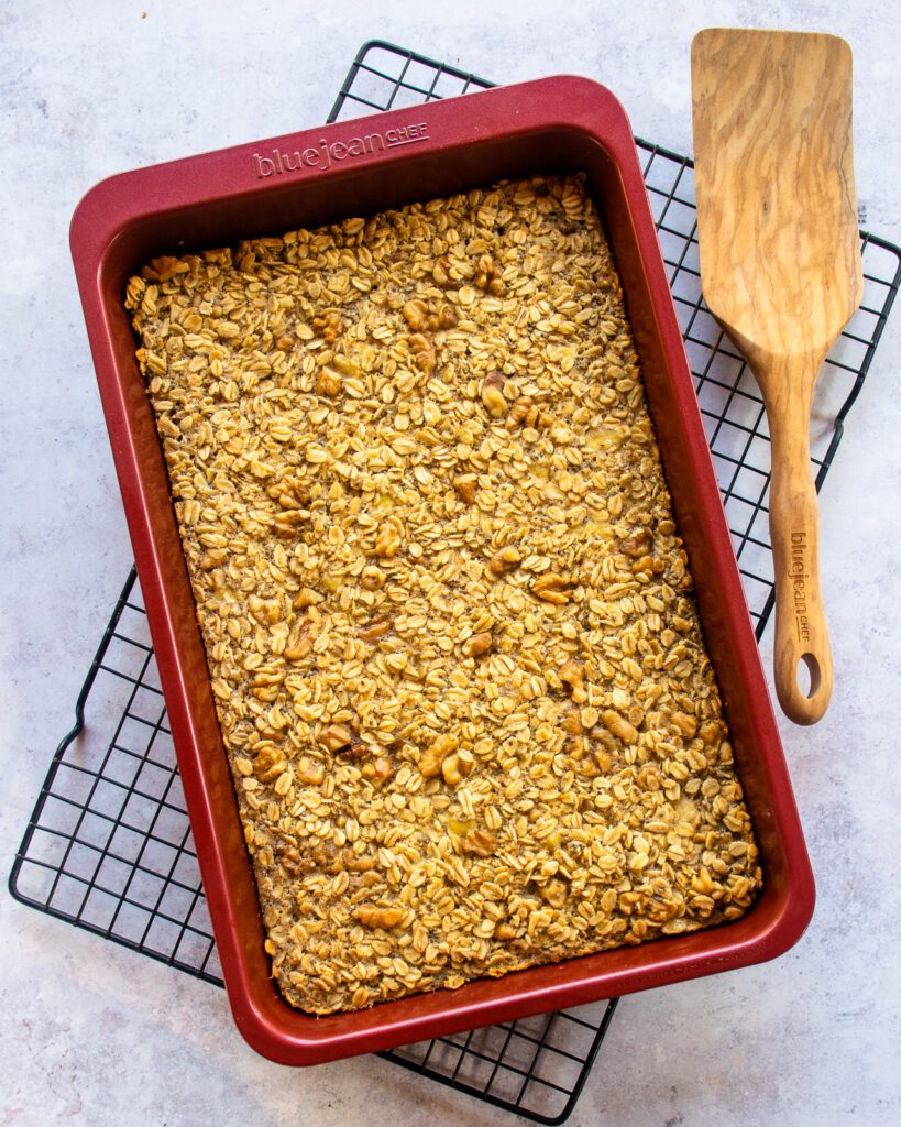 Baked Banana Oatmeal in a red baking pan on a cooling rack with a wooden spoon.