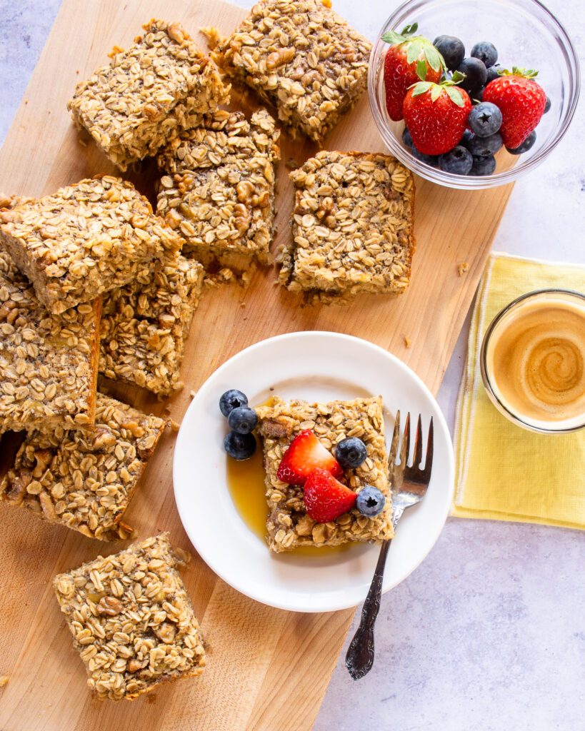 Looking down on baked banana oatmeal squares with one on a plate with maple syrup and berries.