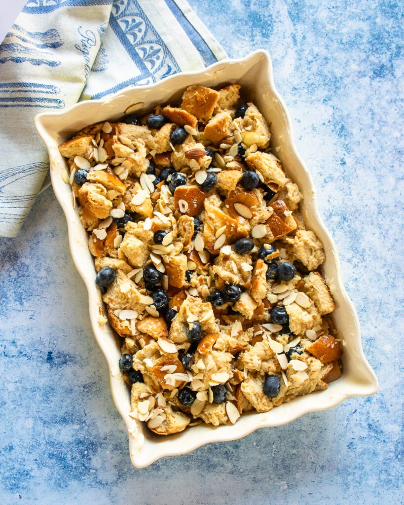 An unbaked blueberry almond bread pudding in a ceramic baker.