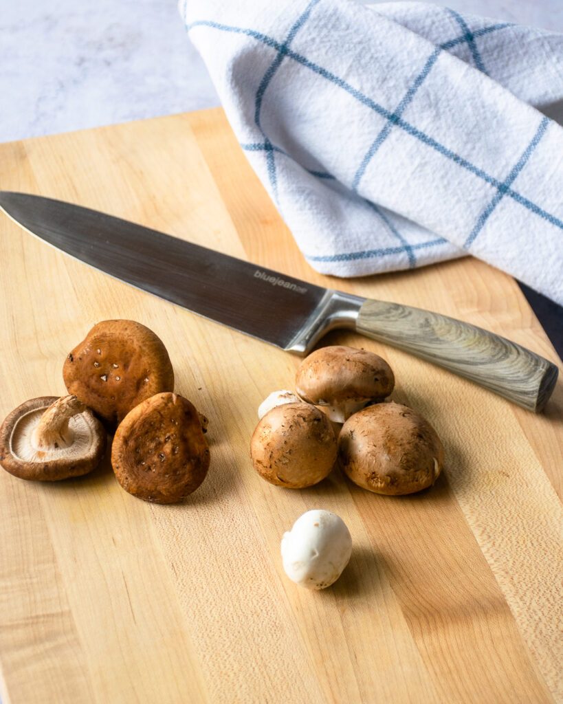 Three different types of mushrooms on a cutting board with a knife.