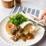 A spoon putting mushroom sauce on a chicken breast.