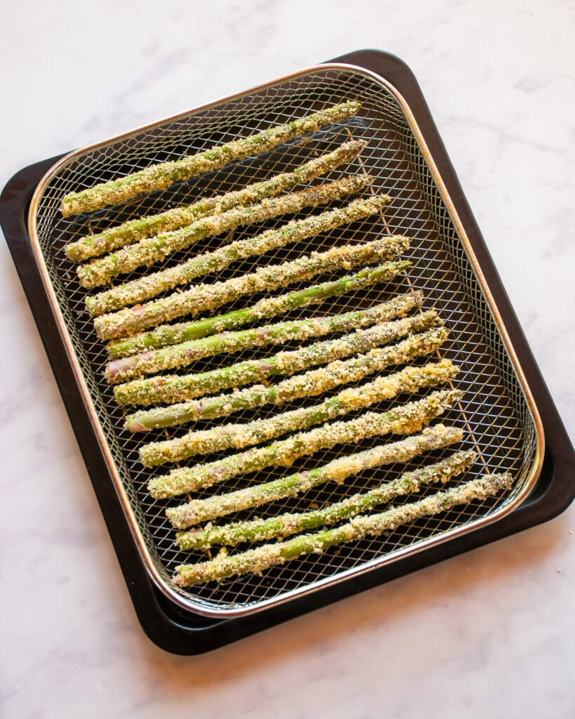 Breaded asparagus in an air fryer basket ready for the air fryer.