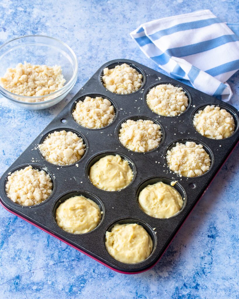 A tray of unbaked muffins with streusel topping on top.