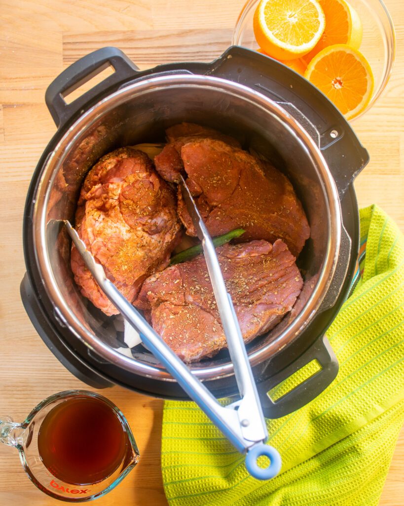 Looking down into a pressure cooker with seasoned pork inside.