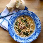 A blue and white bowl with creamy slow cooker beans and some crusty bread.