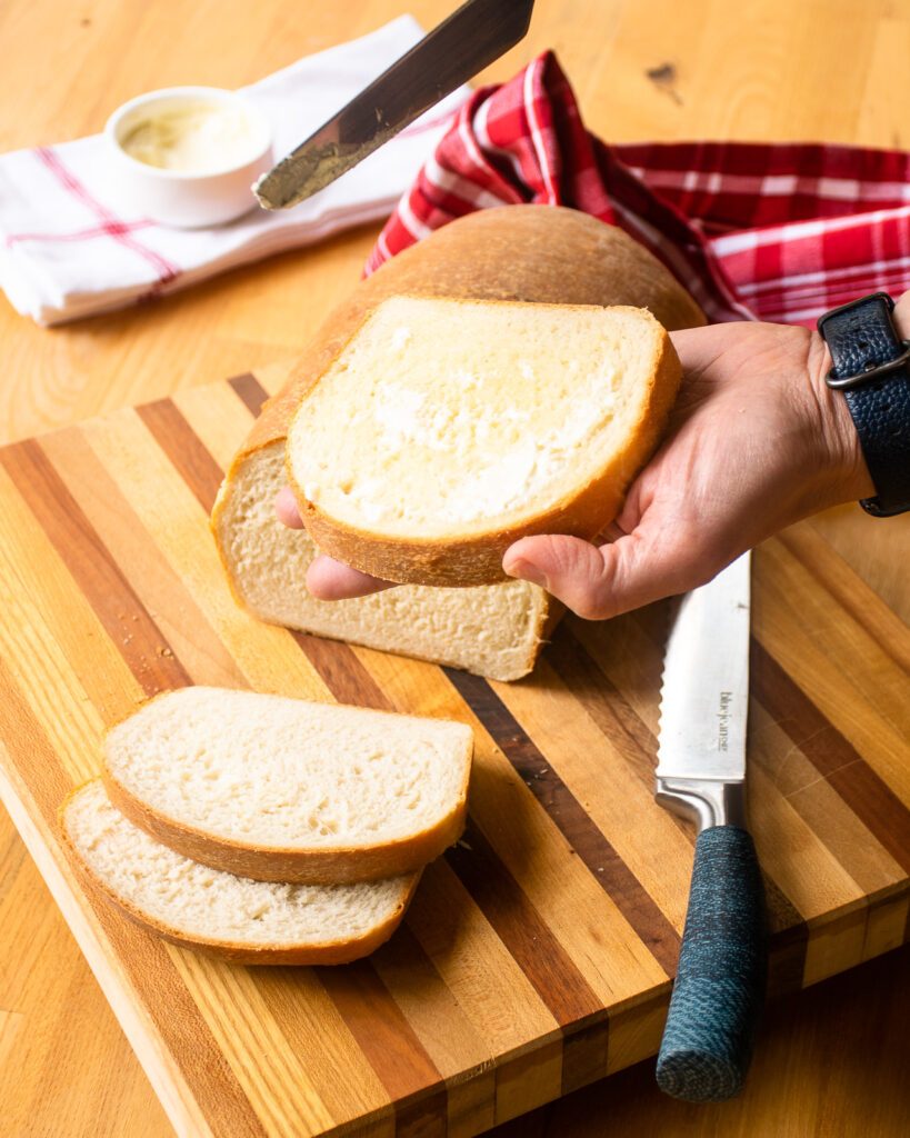 A hand spreading butter on a slice of white sandwich bread.