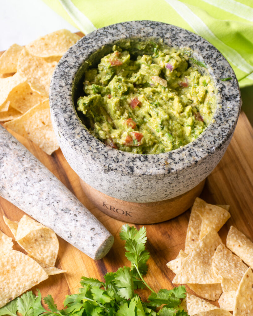 A mortar and pestle with guacamole in the mortar and chips nearby.