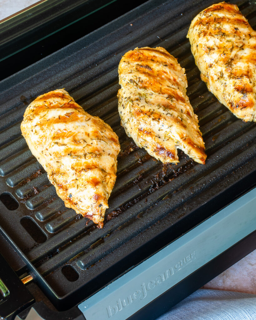 Three chicken breasts grilling on an indoor grill.