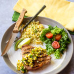 Grilled tuna steaks with corn salsa, rice and a salad on a white plate.